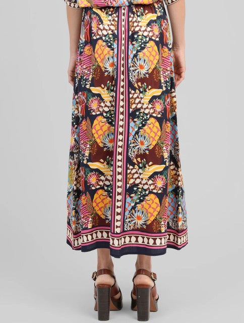 A multicolor tropical pineapple print midi skirt with a decorative border, shown on a model from the back against a light gray background.