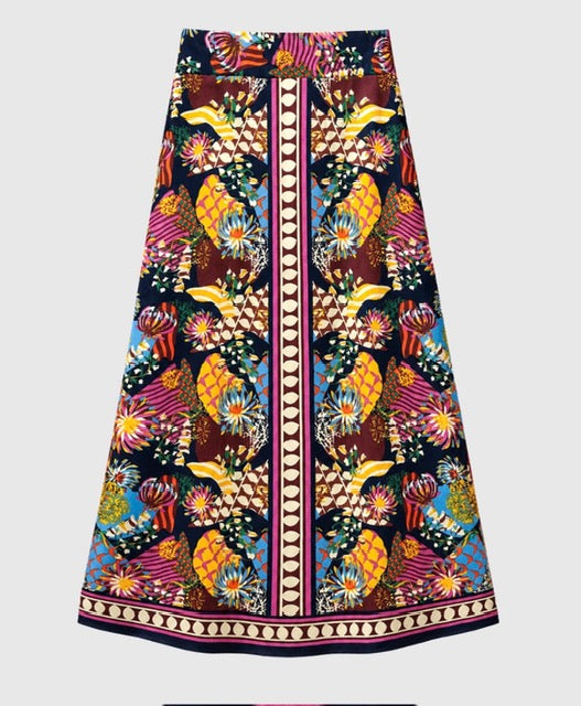 A long A-line midi skirt featuring a vibrant, multicolor batik-style print with birds, flowers, and geometric patterns on a dark background, complete with a central vertical stripe and a decorative border.