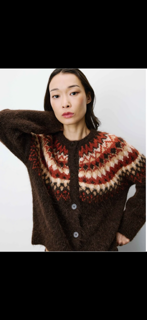 A woman wearing a brown fuzzy knit cardigan sweater with a red, cream, and brown Fair Isle patterned yoke, photographed against a plain light background.
