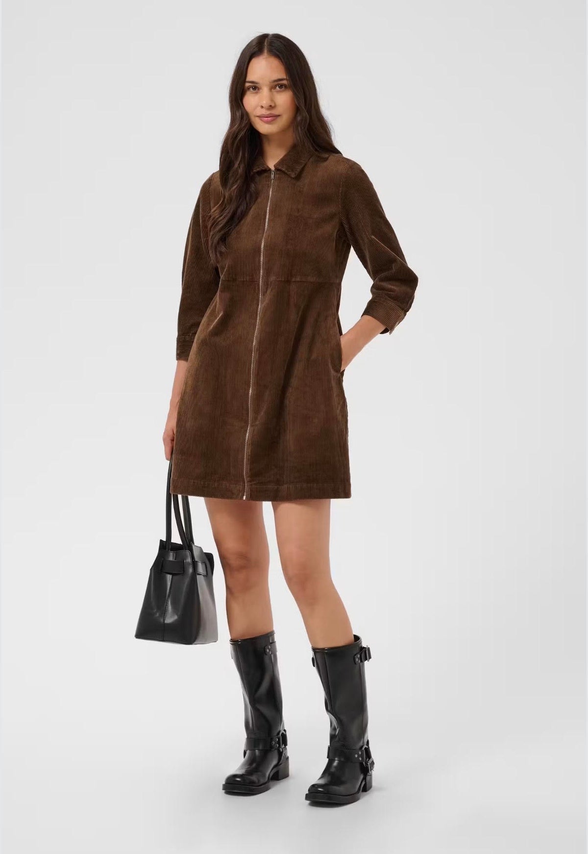 A woman models a brown corduroy zip-front mini coat with a collar, paired with black knee-high boots and a black handbag, against a light gray studio background.