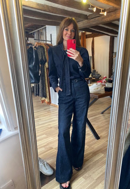 A woman takes a mirror selfie in a boutique showing a dark navy blue outfit consisting of a long-sleeve button-up shirt and matching high-waisted, wide-leg jeans.