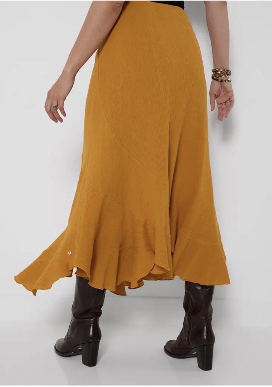 A mustard yellow midi skirt with a ruffled hem, shown on a model from the back wearing dark brown heeled ankle boots against a plain white studio background.
