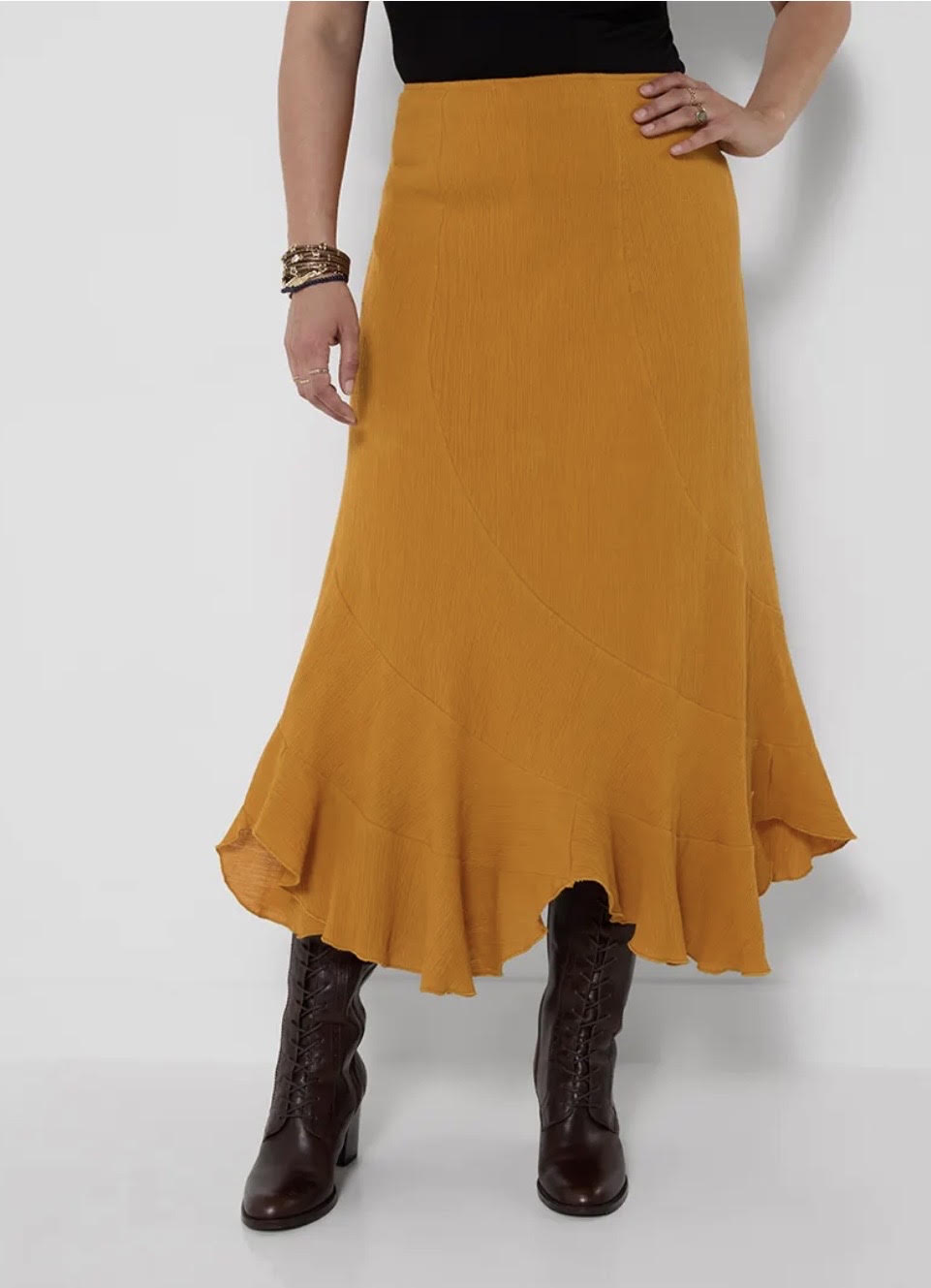 A mustard yellow flared midi skirt worn by a model, styled with a black top and dark brown lace-up ankle boots against a light gray studio background.