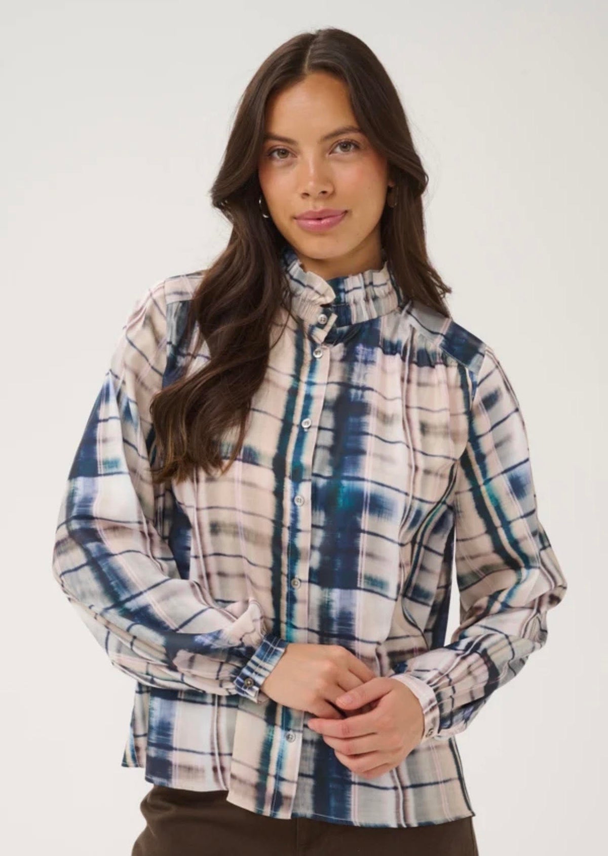 A woman modeling a long-sleeve high-neck plaid blouse with a blue, white, and beige pattern, set against a plain light gray studio background.
