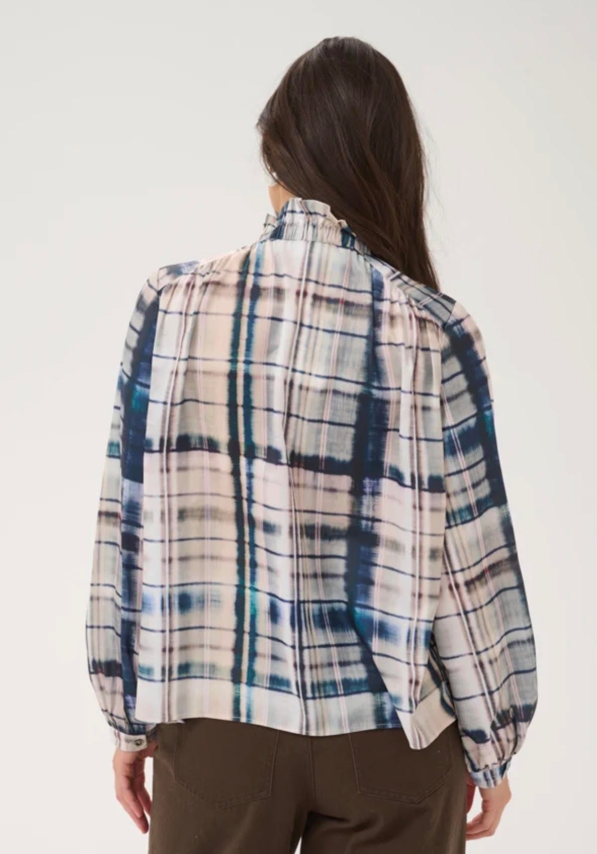 A woman shown from the back wearing a long-sleeve plaid blouse with a high gathered neckline and brown pants, photographed against a plain light background.