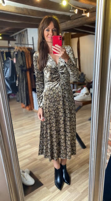 A woman takes a mirror selfie in a boutique wearing a long-sleeve, gathered-waist midi dress with a brown and beige snakeskin pattern, paired with black ankle boots.