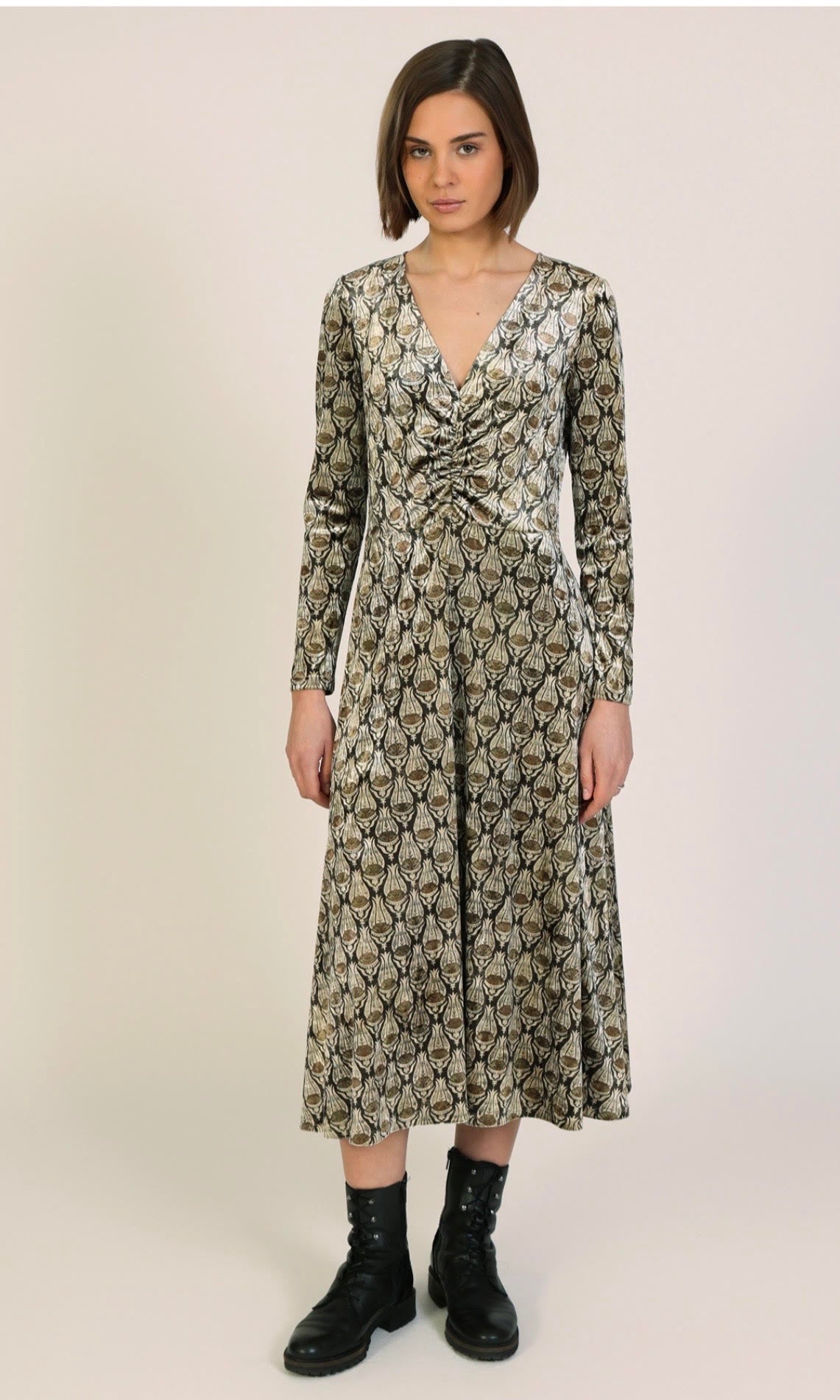 A woman modeling a long-sleeve midi dress with a brown and beige snakeskin pattern, featuring a gathered sweetheart neckline and black lace-up ankle boots, set against a plain light beige studio background.