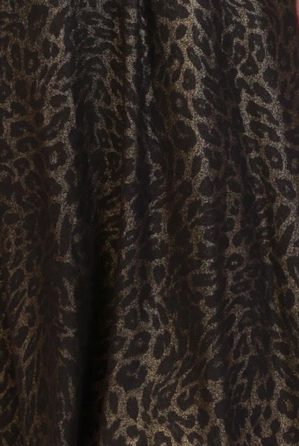 Close-up of a leopard print fabric with a black base and shimmering metallic gold pattern.